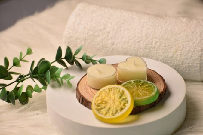 Bougies, rondelles de citron et branches d'eucalyptus disposées sur un support en bois à côté d'une serviette blanche pour une journée spa.